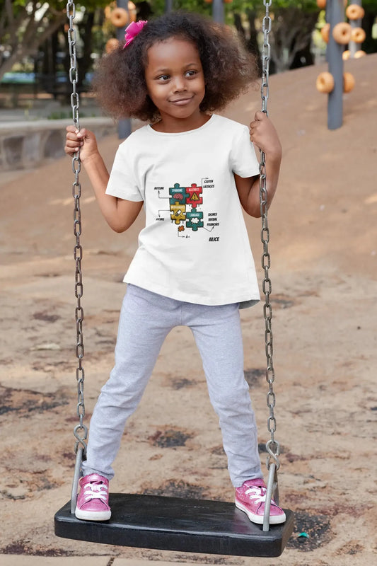 Enfant heureuse en t-shirt autisme blanc personnalisé avec design puzzle, nom Alice et informations vitales sur aire de jeux